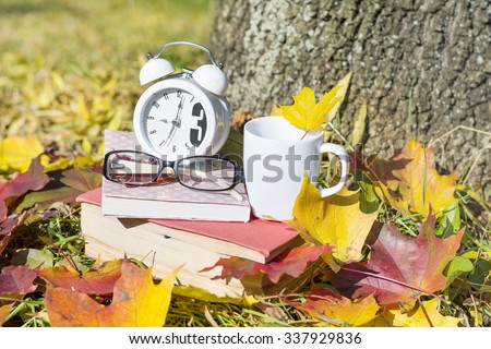 books with coffee cup and clock on a colorful leaves background - autumn concept