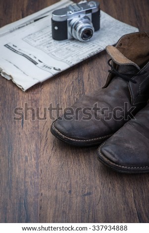 Old worn out brown leather shoes with camera and newspaper over the brown background