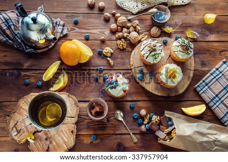 view from above on a wooden table with cupcakes, berries, candies, chocolate, nuts and tea set Royalty-Free Stock Photo #337957904