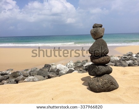 A lava rock cairn on the shore of Kauai at midday with the pacific ocean in the background.