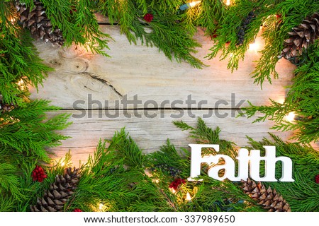 Christmas tree garland border with lights, the word Faith, pine cones and berries on antique rustic wooden background