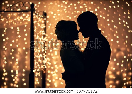 hugs lovers in silhouette against the background of garlands of lights Royalty-Free Stock Photo #337991192