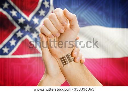 Barcode ID number tatoo on wrist and USA statesl flag on background - Mississippi
