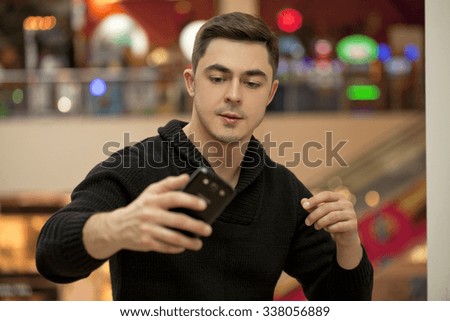 Young handsome man in a black knitted sweater photographing themselves on a cell phone
