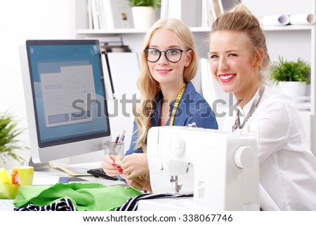 Professional young designers working at fashion studio. Smiling tailor businesswoman working on sewing maching and working while assistant cutting the material for a handmade clothing. Small business