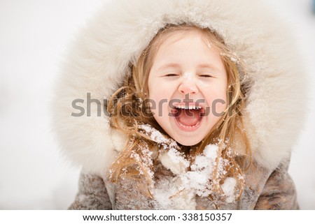 Cute blonde girl with fur around her face laughs because of snow