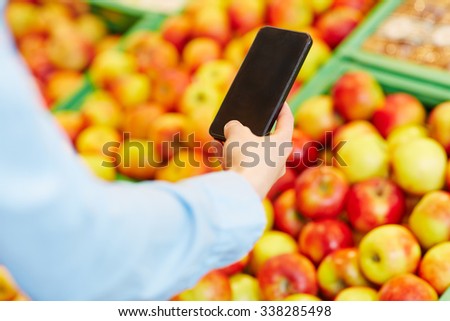 Male hand holding smartphone in front of fruits in a supermarket