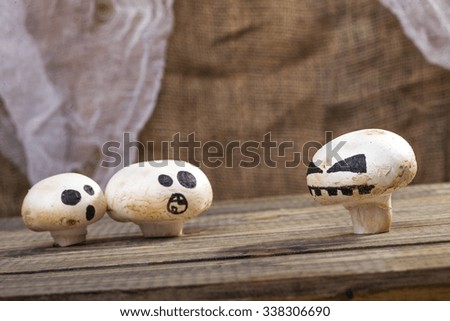 Photo still life set of three Halloween white button mushrooms champignons with ghost face smiles drawn in black felt pen standing on wooden table over blurred rustic background, horizontal picture 