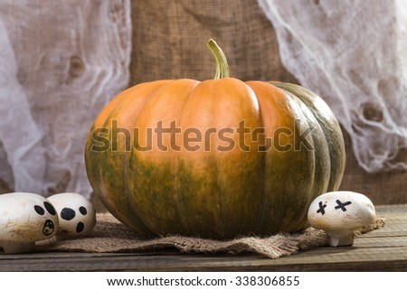 Photo autumn still life one big whole fresh orange green pumpkin with three Halloween champignons with ghost faces drawn in black on sackcloth on wooden table on rustic background, horizontal picture 