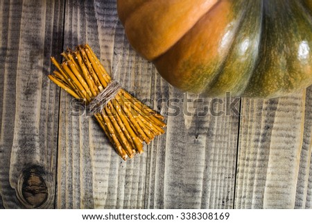 Photo top view sheaf of delicious stick biscuits straws tied together with string and one side of big whole fresh orange pumpkin on wooden table on timber background, horizontal picture 