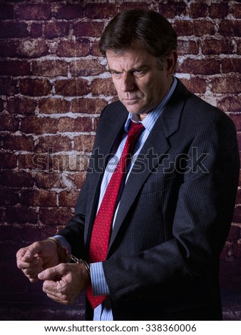 Professional mature business man in business suit with hands in handcuffs showing 