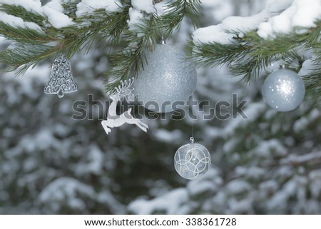 Snowy pine tree branches with sparkling reindeer ornament and Christmas baubles at snowy wood background