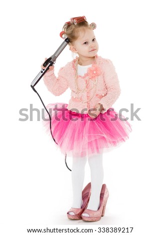Cute little girl with curlers on her head dressed in pink clothes and a huge mother's shoes holds a curling iron on a white background. Little fashionista.  3 year old.