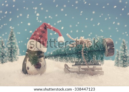 winter scene with snowman in santa hat pulling a sled with christmas tree in vintage style 
