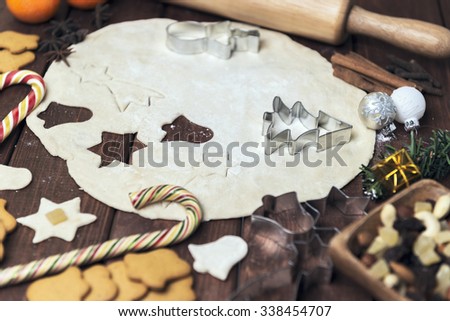 On a wooden desk background Christmas composition - candy cane, dough figurines, Christmas balls, raisins, nuts, cinnamon sticks, cookies, anise, mandarins; bump; roll out the dough layer; plunger