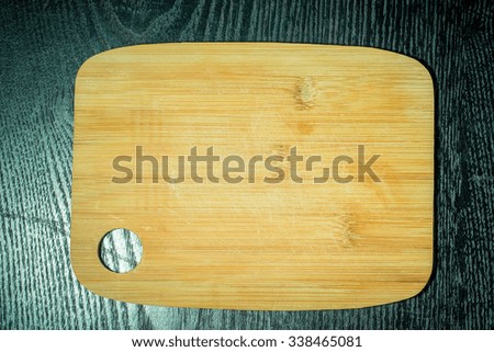 Modern light wooden cutting board with ring hole on a black table like background. Space for text. Toned.