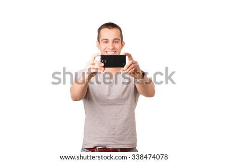 Smiley Caucasian young man is wearing a grey t-shirt and taking a selfie with a black smartphone.