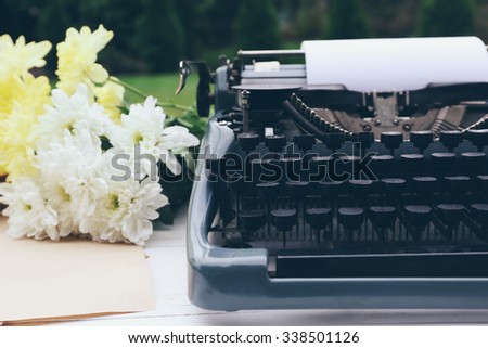 Vintage black typewriter with papers and flowers on wooden table, outdoors