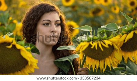 Beautiful young brunette woman is standing among sunflowers. Color effects, custom white balance used on this picture.