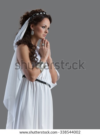 Portrait of a woman praying in a white dress of ancient Greek style on the gray background

