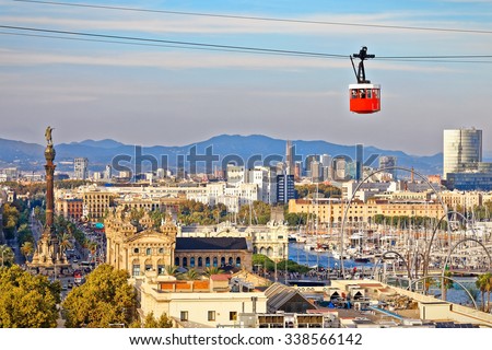 Red cabin of cableway stands out on Barcelona's port, indicated by the statue of Christopher Columbus