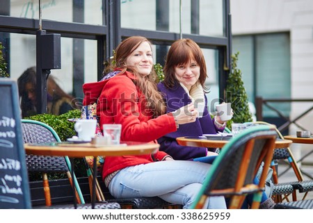 Two cheerful girls drinking coffee and chatting in a Parisian street cafe