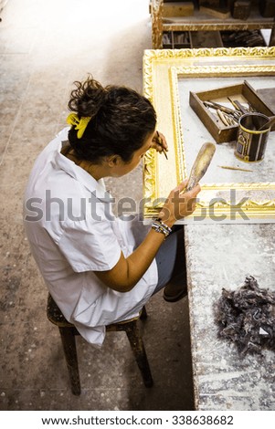 Female artisan working on the decoration of a big wooden picture frame. View from above. Slight vignetting effect. Selective focus on the hands.