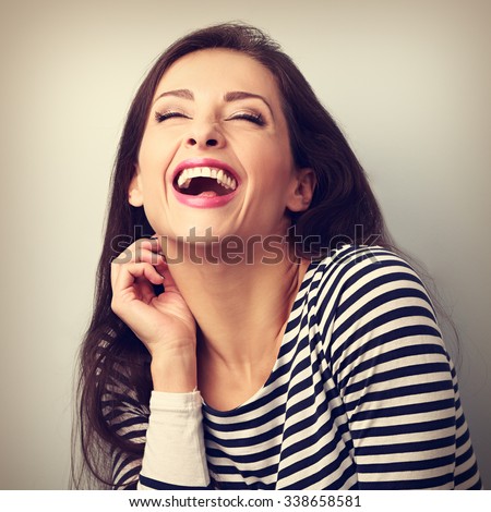 Laughing young casual woman with wide open mouth and closed eyes on blue background