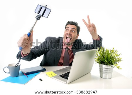young attractive businessman in suit and tie working at office desk taking selfie photo with mobile phone camera and stick posing crazy happy and successful isolated on white background