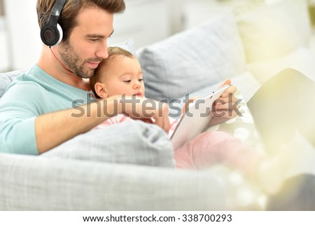 Daddy and baby girl in sofa using tablet and headphones