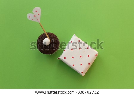 Polka dot gift box and cupcake with polka dot heart stick on green background
