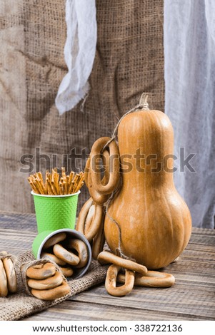 Still life big gourd with bunches bind with string lying on sackcloth two disposable green cups with straws and hard oval cracknels standing on wooden table on rustic background, vertical picture 