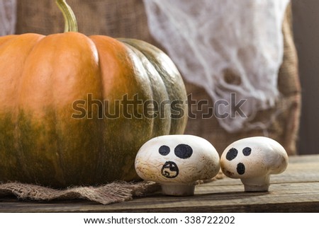 Photo autumn still life one big whole fresh orange green pumpkin with two Halloween champignons with ghost faces drawn in black on sackcloth on wooden table on rustic background, horizontal picture 