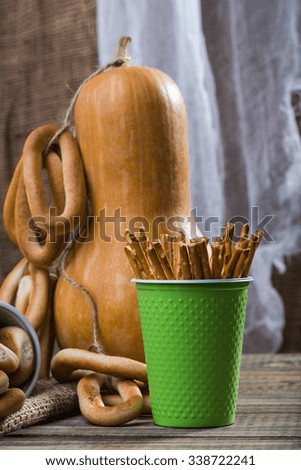 Still life closeup one big gourd with bunches of hard oval cracknels bind with string and disposable green cup with straws standing on wooden table on blurred rustic background, vertical picture 