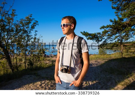 young handsome man with backpack and retro camera on the beach