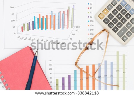 Business concept : Pen placed on notebook with glasses and calculator on graph background.