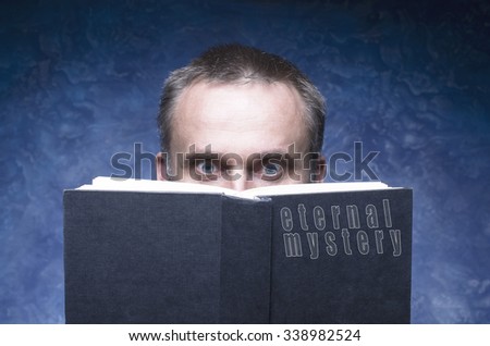 Eternal mystery written on the cover of the book, mature man being focused and hooked by book, reading open book, man behind book.