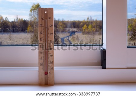 Thermometer on the plastic window and sunny autumn landscape in the background