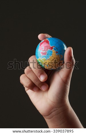 A kid's hand holding a globe in a dark background