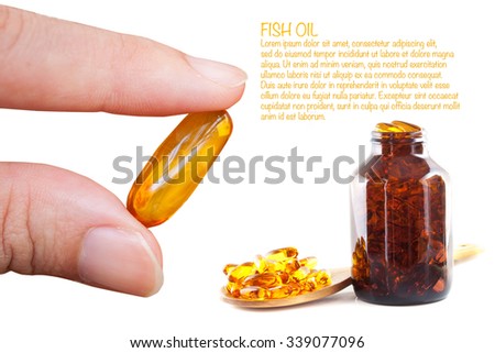 Hand holding a Fish oil capsule with bottle of pills in the background