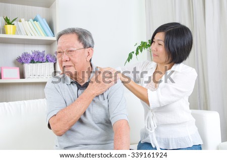 Asian old man shoulder pain, sitting on sofa , daughter massaging father shoulder. Chinese family, senior retiree indoors living lifestyle at home. Royalty-Free Stock Photo #339161924