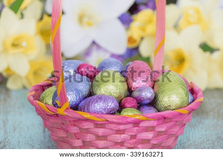 Pastel color chocolate eggs in a pink Easter basket, spring flowers in the background