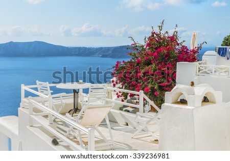White cozy terrace with red flowers( on a plant )above the Mediterranean sea, with beautiful view of the Caldera and Therasia.Scenic natural landscape.Santorini (Thira) island.Cyclades.Greece.Europe. 
