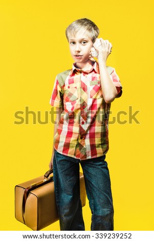 Funny child traveler wearing stylish clothes holding a small suitcase and a seashell going on summer vacation. Vintage effect.