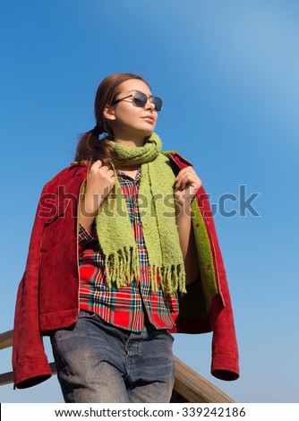 Autumn Fashion close up portrait of young woman walking outdoor,wearing red lether coat,red checkered shirt,green scarf and sunglasses,smiling,positive emotions
