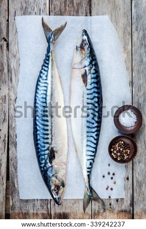 Two raw fresh mackerel fishes on a paper with salt and pepper on wooden table