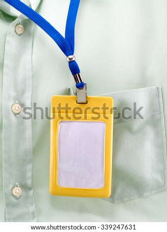 blank ID badge or staff identity name tag hanging attached to green shirt pocket, close-up personal neck name tag in yellow plastic holder for your simple text, vertical image
