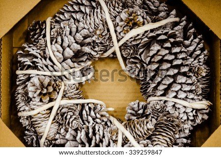Picture of beautiful rustic christmas pine cones wreath. Closeup of charming decor in cardboard box on blurred indoor background.
