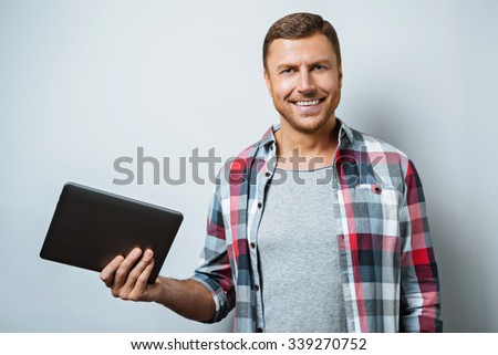 Studio shot of handsome young man on grey background. Man smiling and holding tablet computer