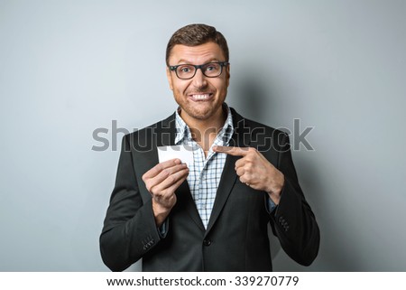Fun photo of handsome young businessman on grey background. Man wearing jacket and shirt. Man smiling and showing visit card